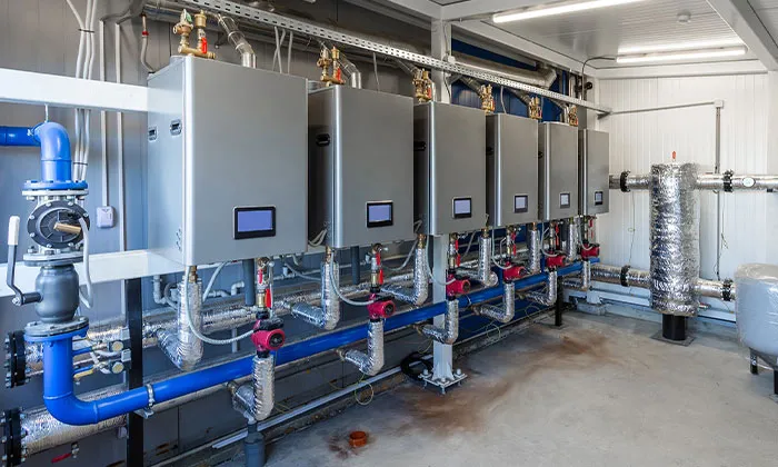Commercial mechanical room with six wall-mounted tankless boilers, insulated pipes and red circulation pumps