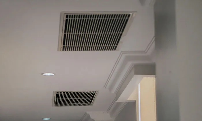 Two rectangular ceiling HVAC vents and recessed light above decorative crown molding in interior ceiling