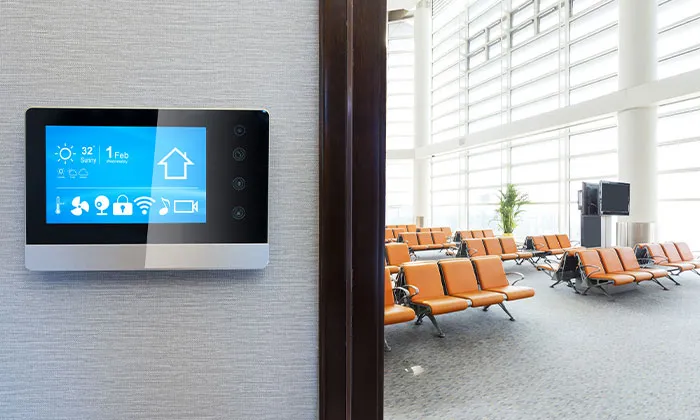 Smart digital control panel on wall beside bright airport terminal lounge with orange seating and floor-to-ceiling windows